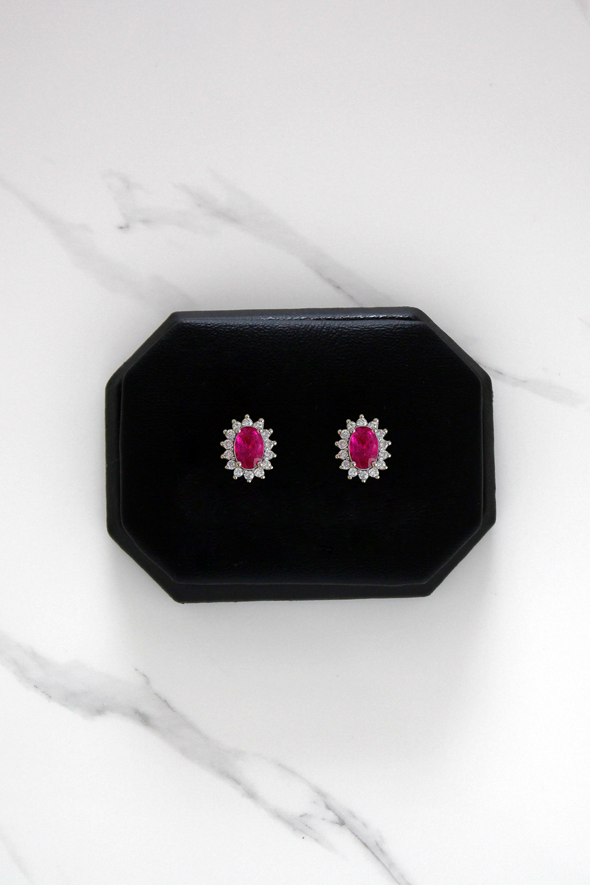 Pair of earrings with ruby gemstones in a black display case on a white marble surface