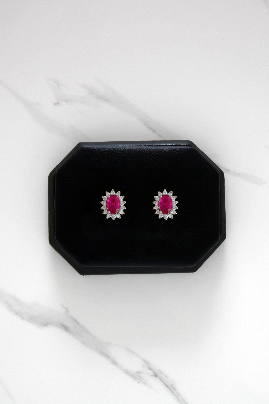 Pair of earrings with ruby gemstones in a black display case on a white marble surface